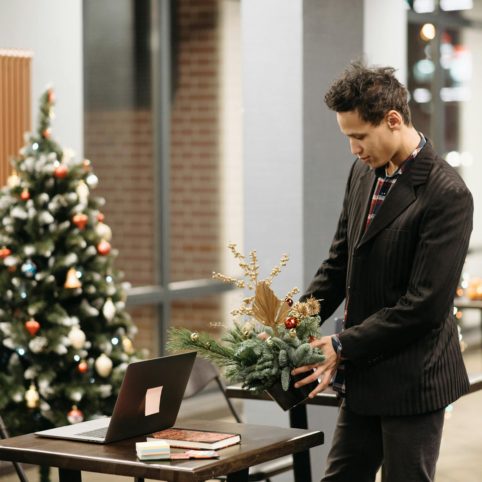 Man arranging a Christmas wreath in an office setting with a decorated tree in the background.